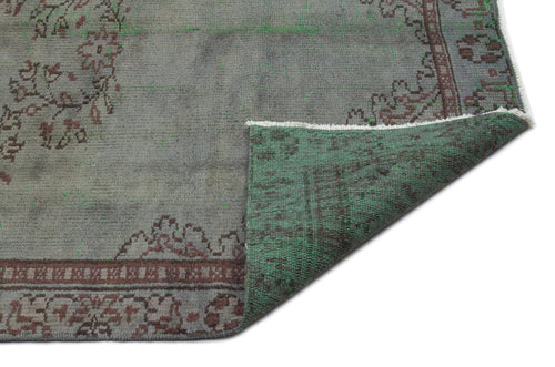 Load image 1 in gallery view. Grey and green distressed rug with a traditional floral border, shown with a corner folded over on a white background.