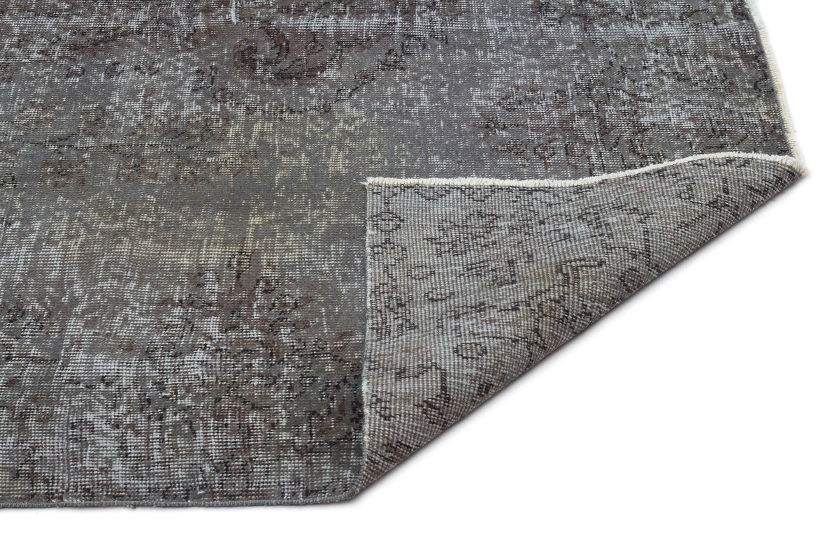 Charcoal and grey distressed rug with a faded traditional medallion pattern, shown with a corner folded over.