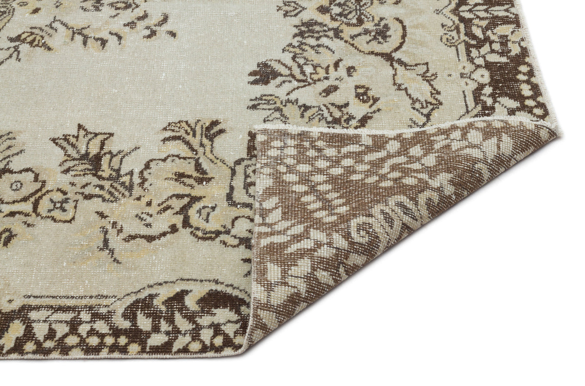 Beige and brown distressed rug with a floral medallion pattern, shown with a corner folded to reveal the woven backing.