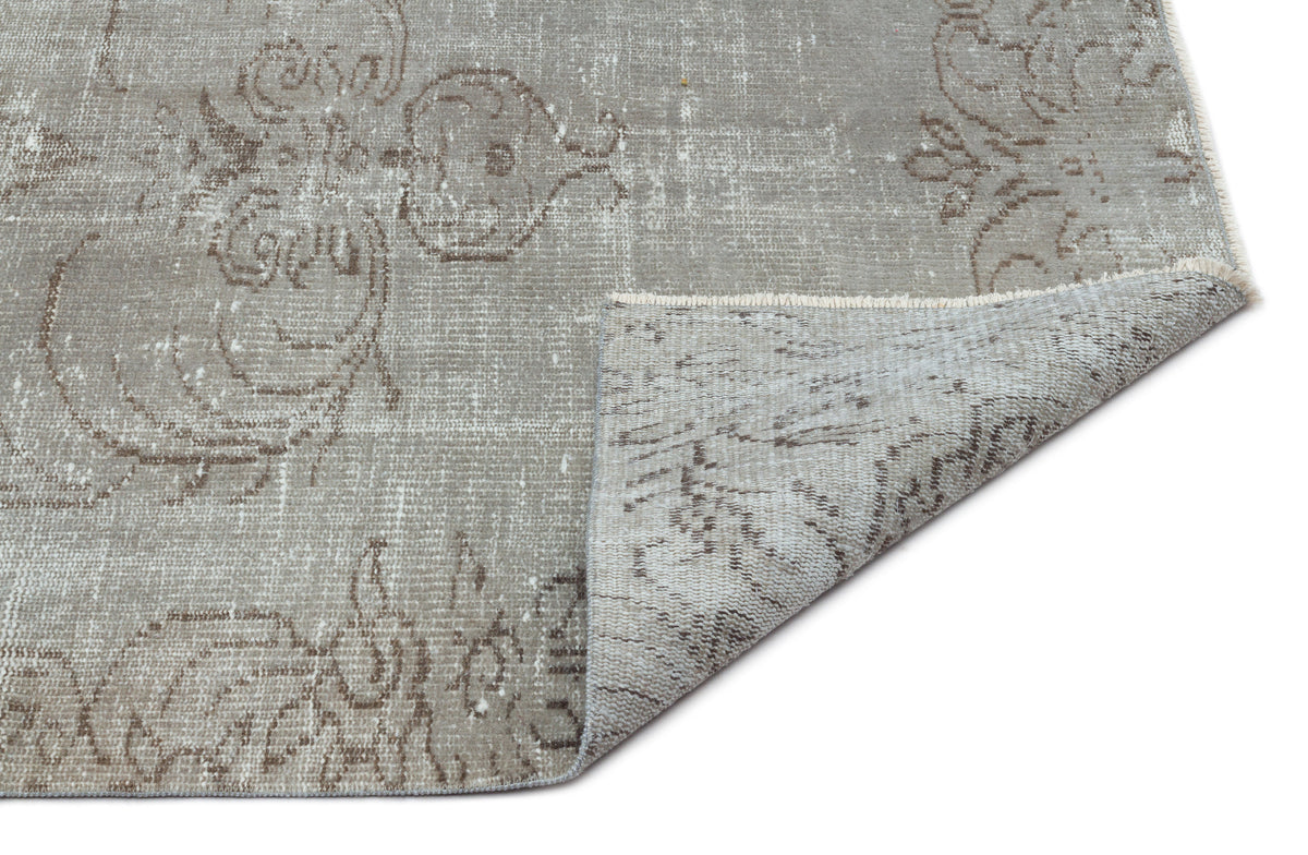 Grey and taupe distressed rug with a faded floral medallion pattern, shown with a corner folded to reveal the backing.
