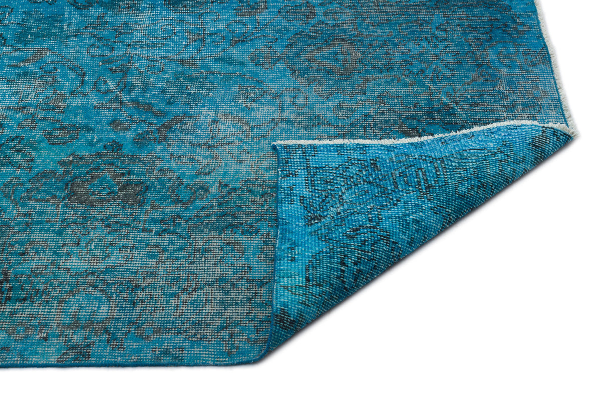 Bright blue distressed rug with a dark grey traditional medallion pattern and a folded corner on a white background.
