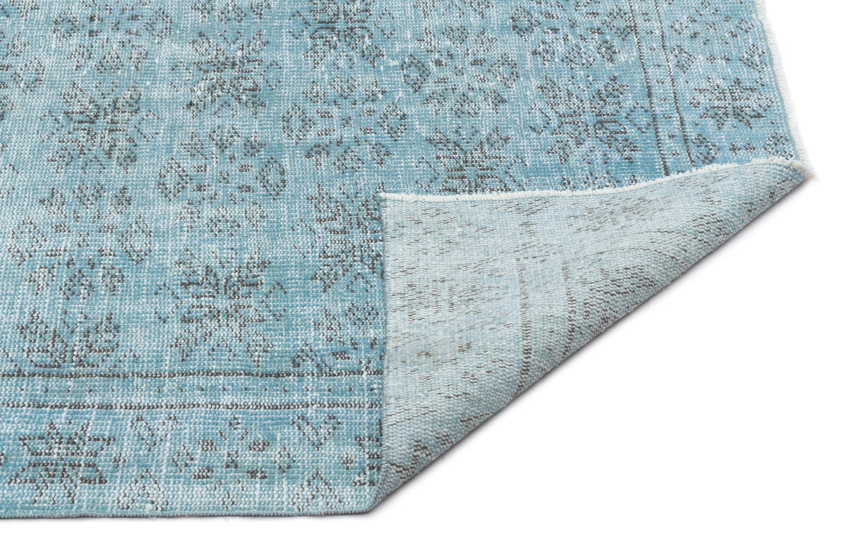 Light blue and grey distressed traditional medallion rug with a folded corner showing the backing.