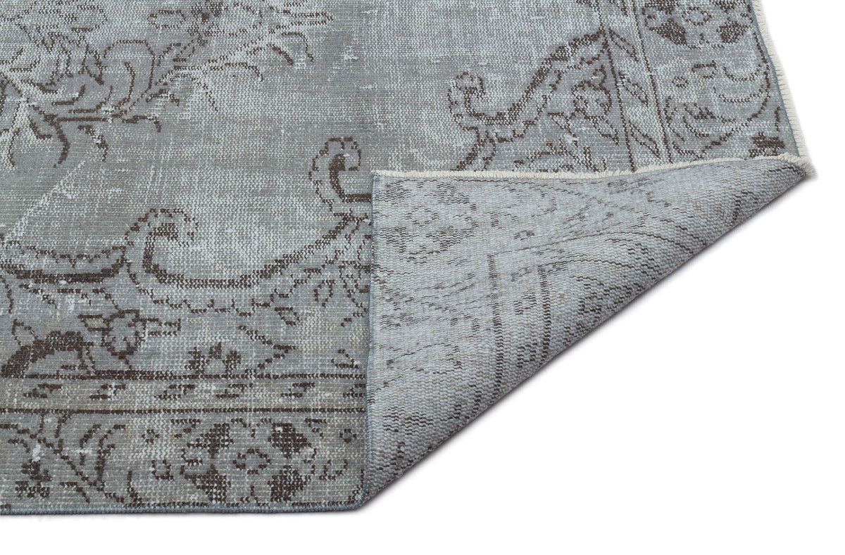 Grey and brown distressed traditional rug with a floral medallion pattern, shown with a corner folded over.