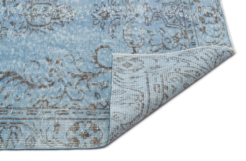 Load image 1 in gallery view. Light blue and grey distressed rug with a traditional floral medallion pattern, shown with a corner folded over.