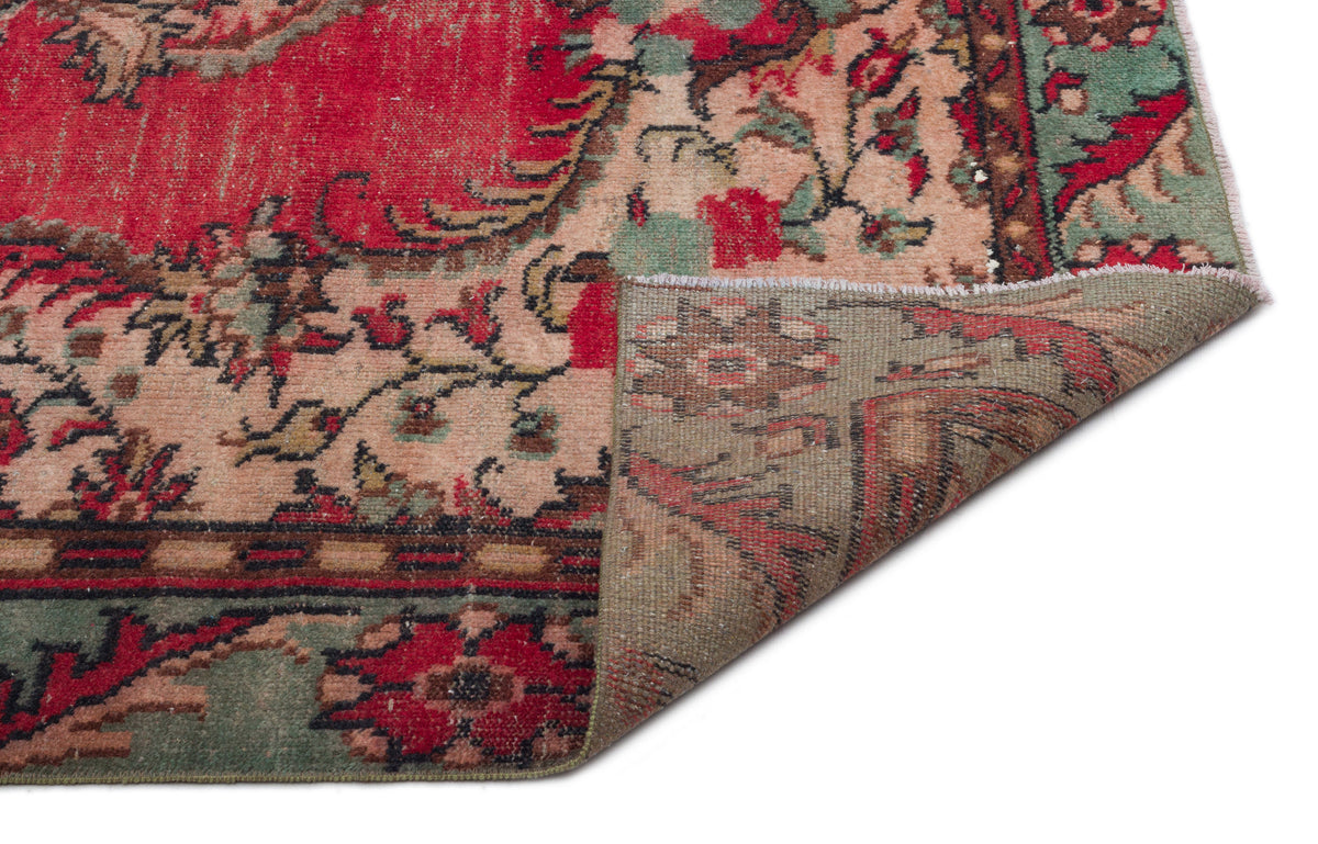 Red, green, and beige vintage-style rug with a floral medallion pattern, shown with a corner folded over.