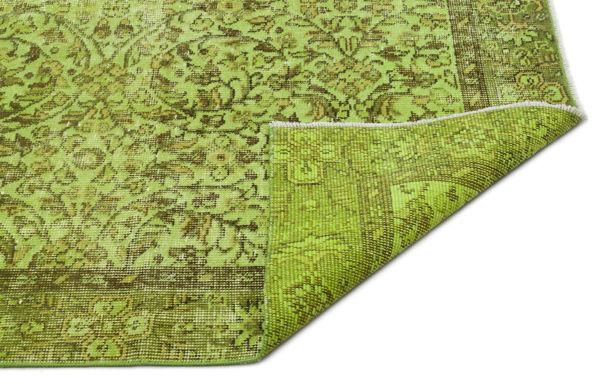 Lime green and brown distressed rug with a traditional floral medallion pattern and a folded corner.