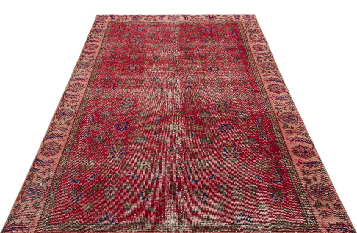 Distressed red Persian-style rug with a faded floral medallion pattern and a wide, muted pink border.