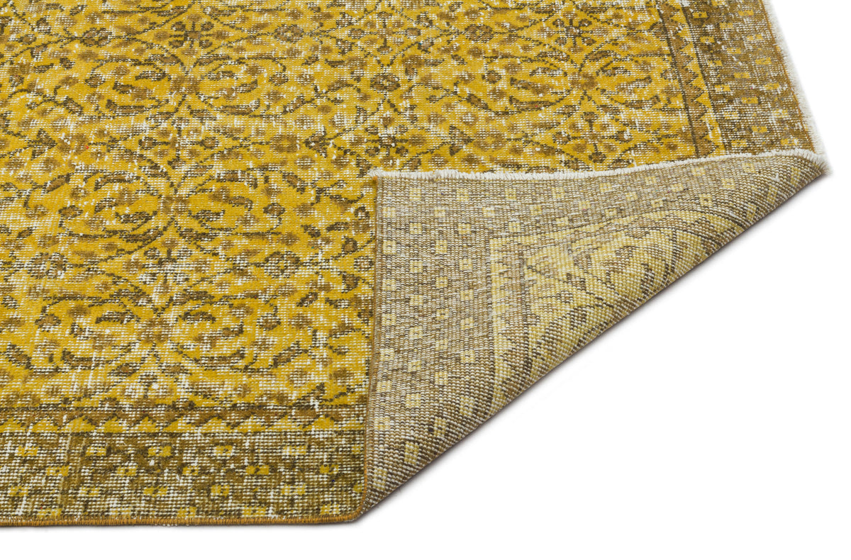 Mustard yellow and brown distressed rug with a traditional floral medallion pattern, shown with a corner folded over.