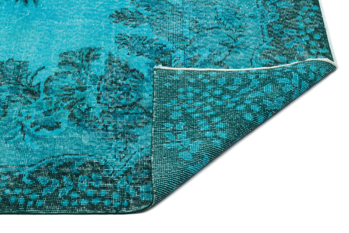 Bright turquoise and dark teal rug with a distressed floral pattern, shown with a corner folded to reveal the backing.