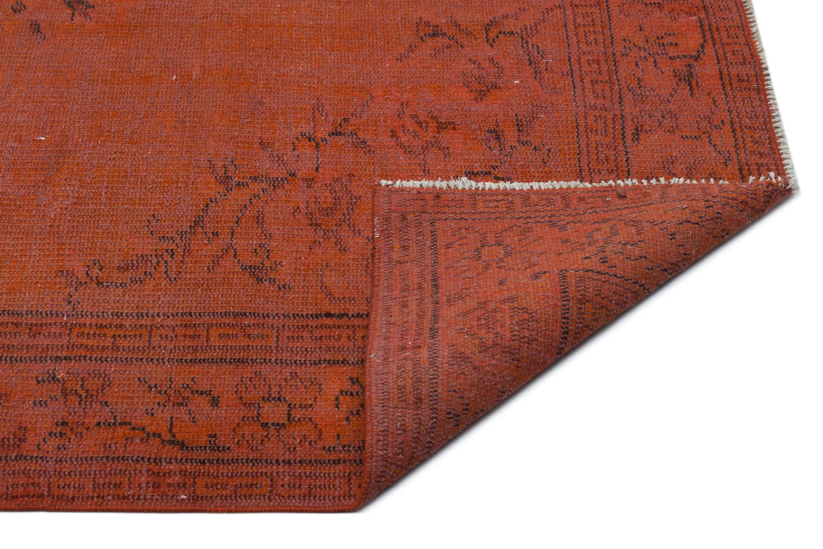 Terracotta red rug with a black floral border and geometric pattern, shown with a corner folded over on a white background.
