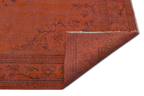 Load image 1 in gallery view. Terracotta red rug with a black floral border and geometric pattern, shown with a corner folded over on a white background.