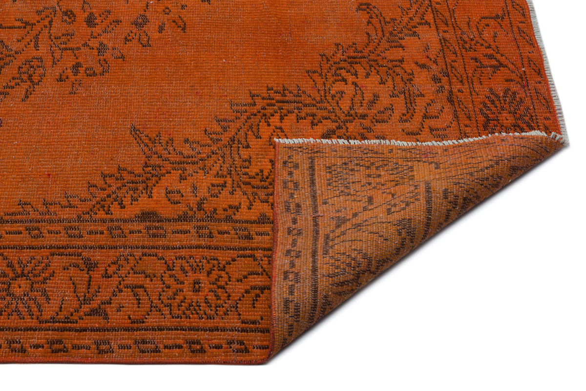 Burnt orange rug with a dark brown floral medallion pattern and a folded corner showing the underside.