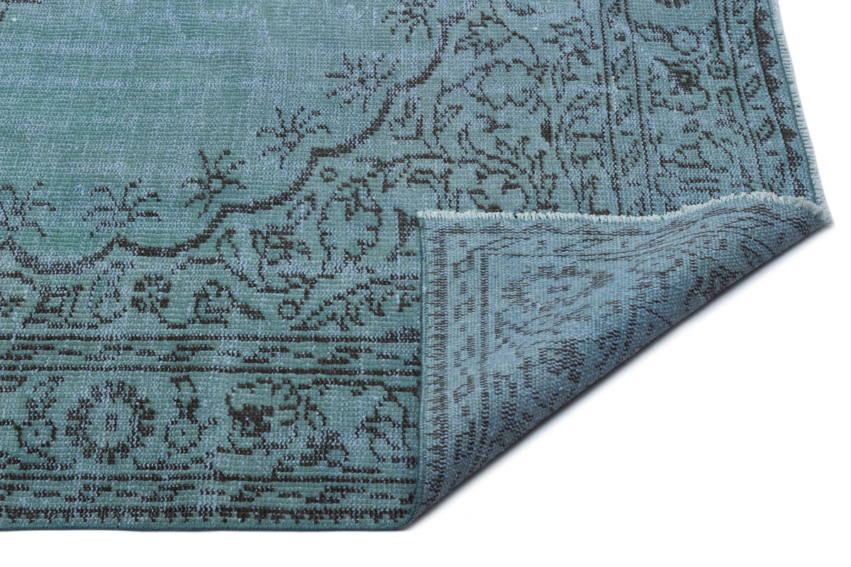 Teal and charcoal distressed rug with a traditional floral medallion pattern, shown with a folded corner.
