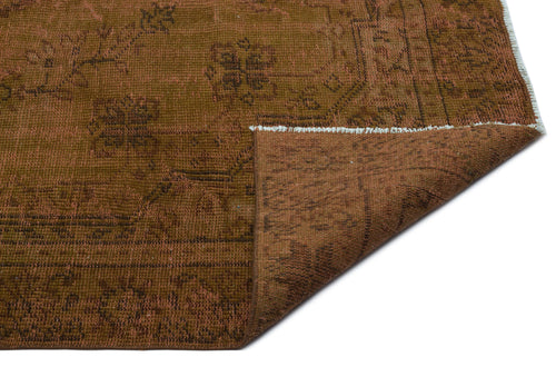 Load image 1 in gallery view. Brown distressed vintage-style rug with a faded floral medallion pattern and a folded corner showing white fringe.
