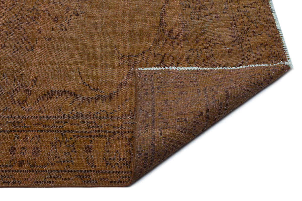 Rust-colored vintage-style rug with a faded dark brown floral pattern and a folded corner showing the underside.
