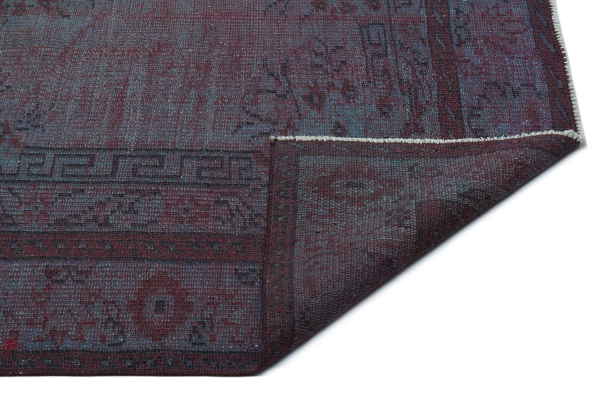 Deep burgundy and slate blue distressed rug with a geometric border pattern, shown with a folded corner.