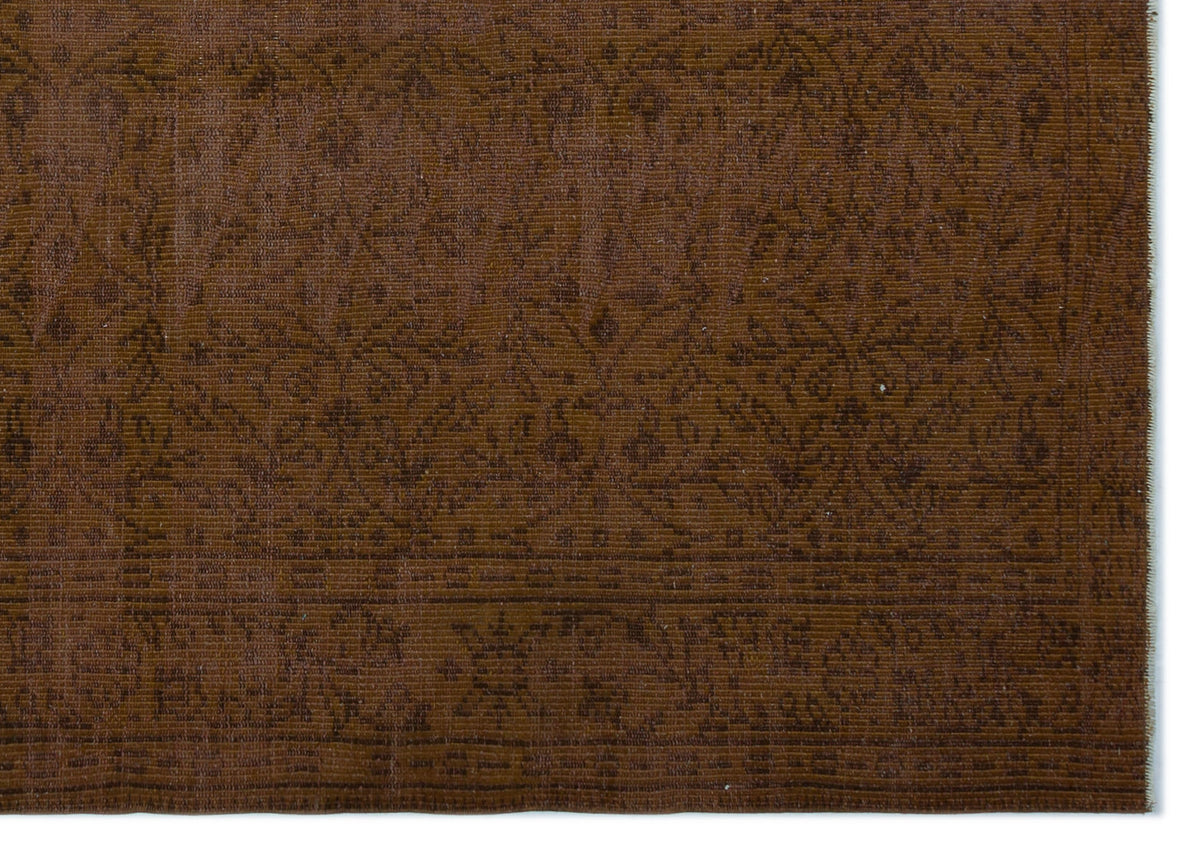 Dark brown rug with a tonal, distressed floral medallion pattern and a decorative border.