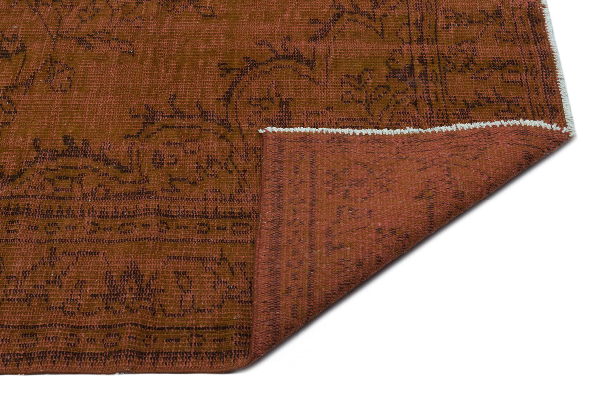 Rust-colored rug with a dark brown floral pattern and a folded corner revealing the solid-colored underside.