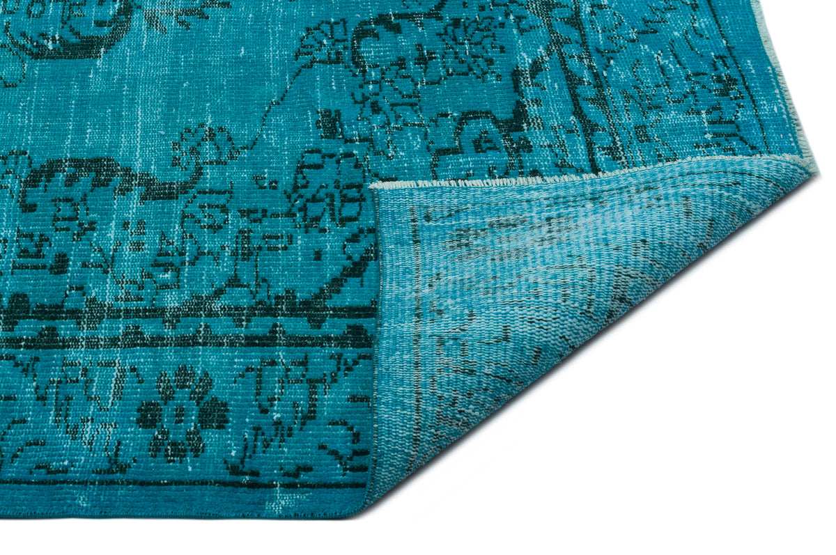 Turquoise and black distressed vintage-style rug with a floral medallion pattern, shown with a folded corner.