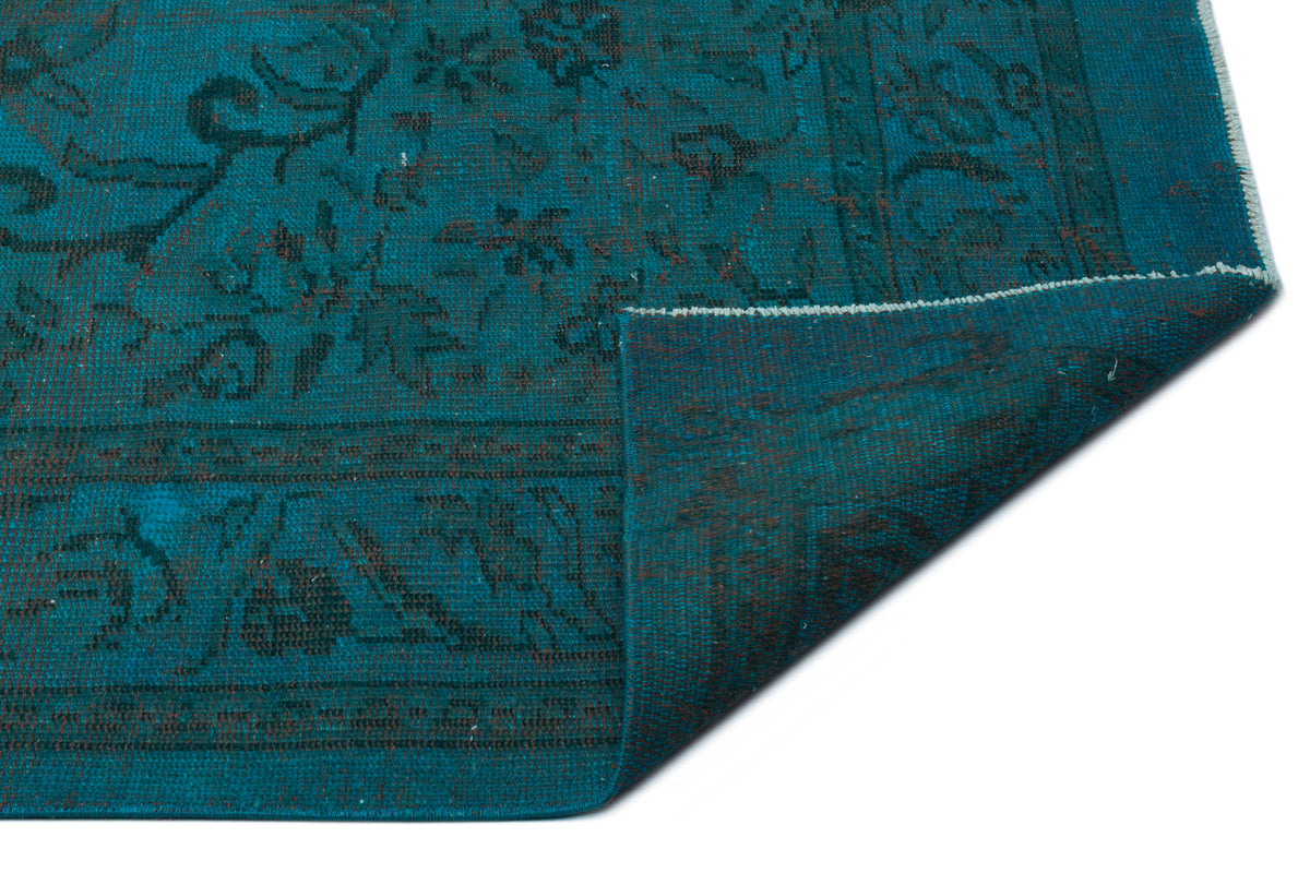 Teal and black distressed rug with a traditional floral pattern, shown with a corner folded over on a white background.