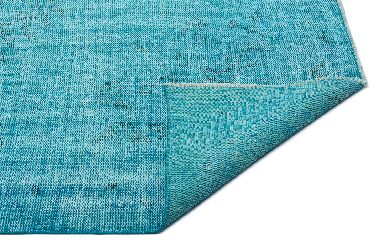 Bright turquoise rug with a distressed, faded pattern and a folded corner showing the woven backing.
