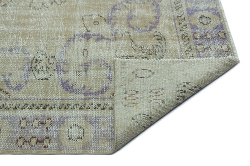 Load image 1 in gallery view. Beige and lavender distressed rug with a floral medallion pattern, shown with a corner folded to reveal the backing.