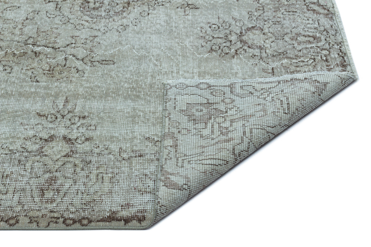 Light gray and brown distressed rug with a faded floral medallion pattern, shown with a corner folded over.