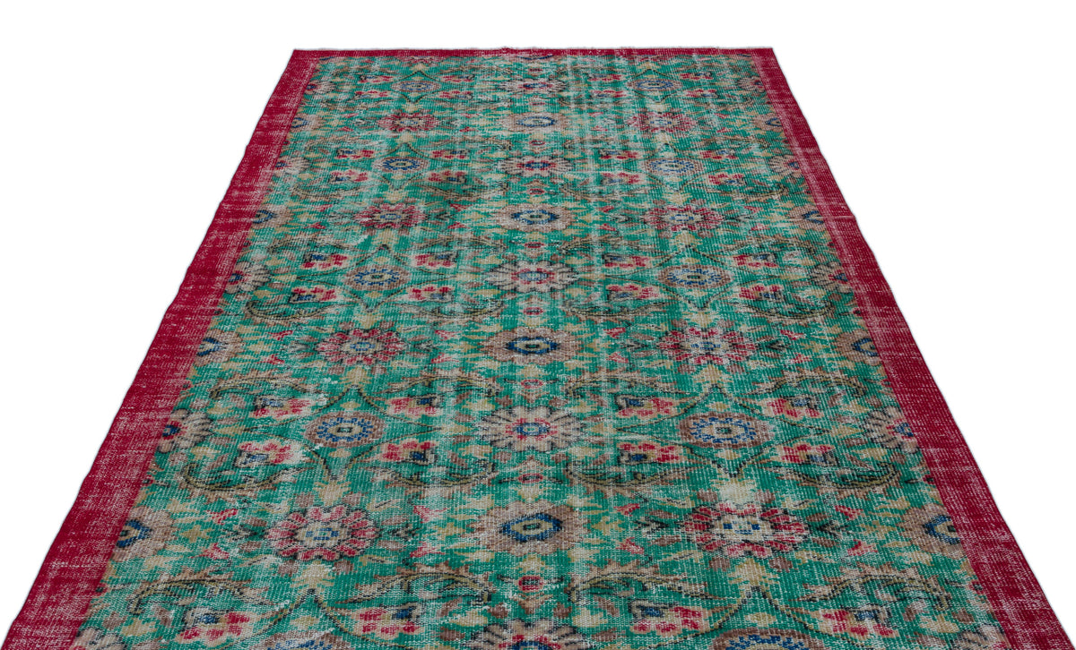 Distressed emerald green rug with a red border and a repeating floral medallion pattern.