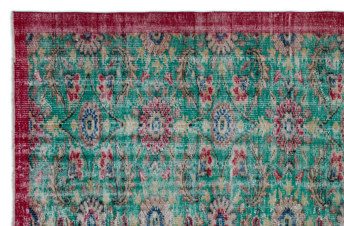 Distressed emerald green rug with a red border and a repeating floral medallion pattern in red, blue, and beige.