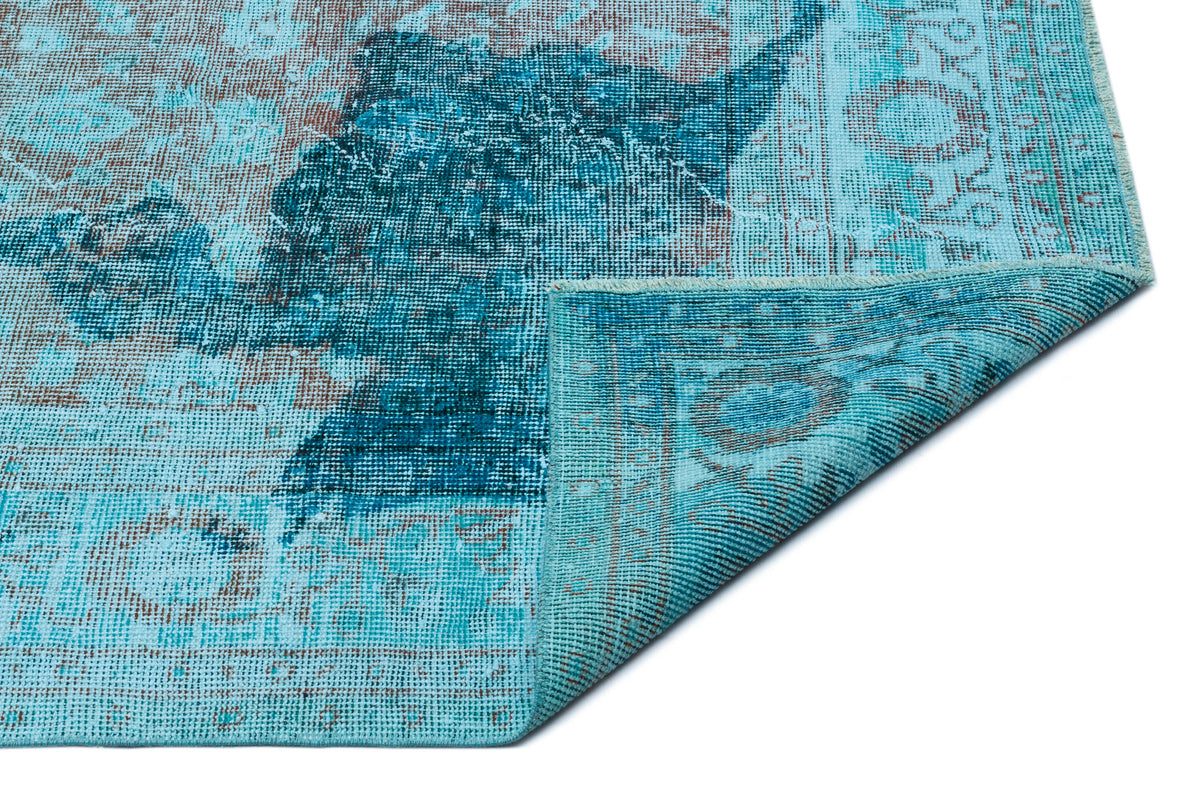 Distressed turquoise and brown vintage-style rug with a faded medallion pattern, shown with a corner folded over.