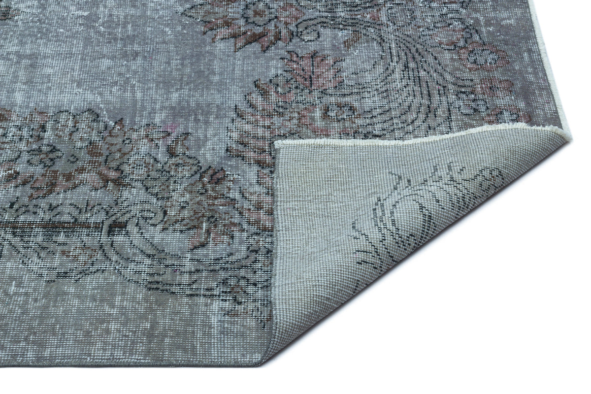 Distressed grey rug with a faded floral medallion pattern and a corner folded over to show the woven backing.