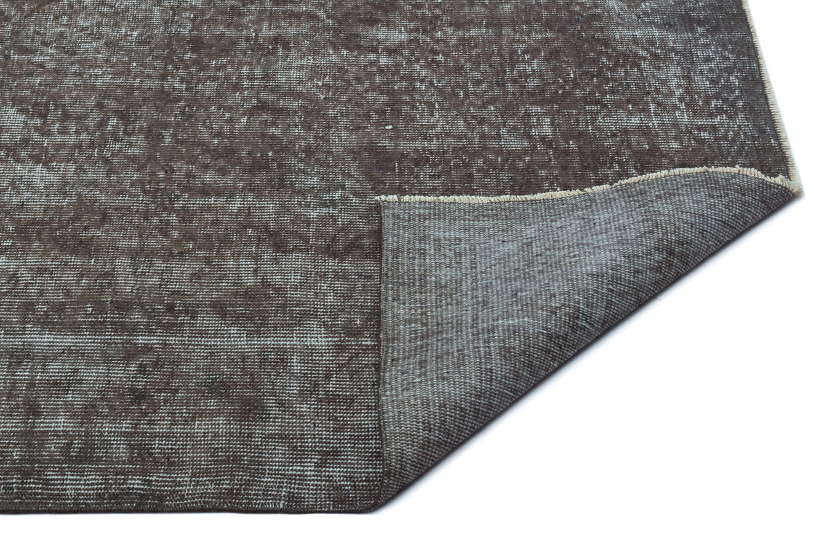 Dark brown distressed rug with a faded texture and a corner folded over to reveal the woven backing.