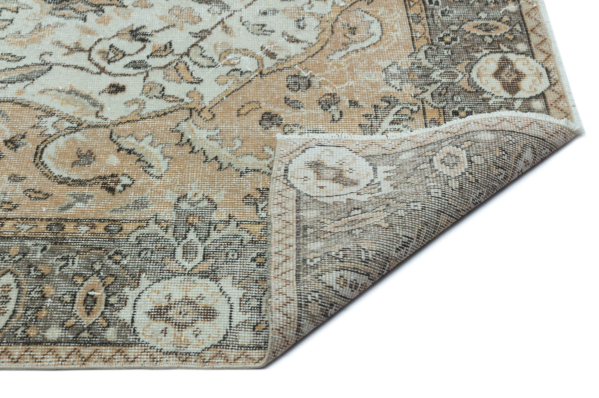 Tan, cream, and charcoal distressed traditional rug with a floral medallion pattern, shown with a folded corner.