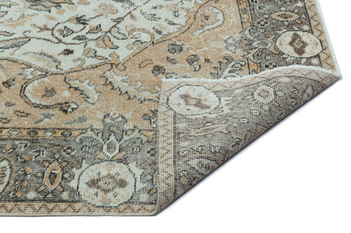 Load image 1 in gallery view. Tan, cream, and charcoal distressed traditional rug with a floral medallion pattern, shown with a folded corner.