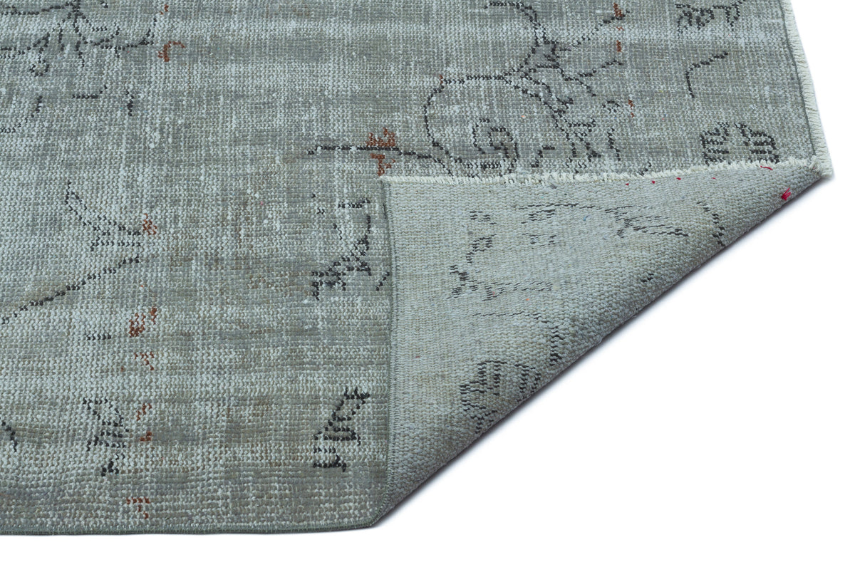 Grey distressed rug with a faded floral pattern and small rust-colored accents, shown with a corner folded over.