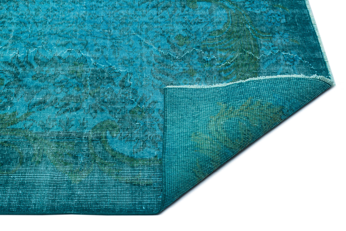 Teal and dark green distressed medallion rug with a folded corner, isolated on a white background.