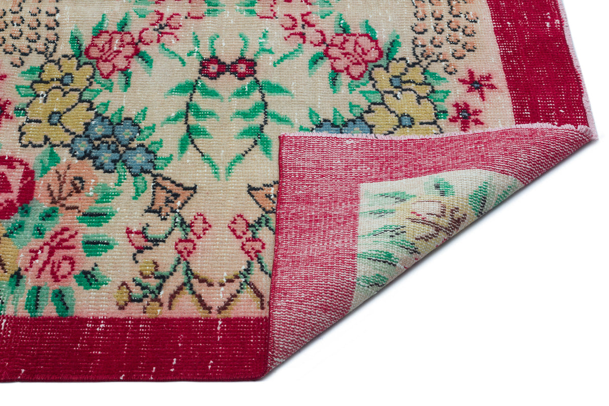 Beige vintage rug with a floral pattern in red, green, and blue, featuring a wide red border and a folded corner.