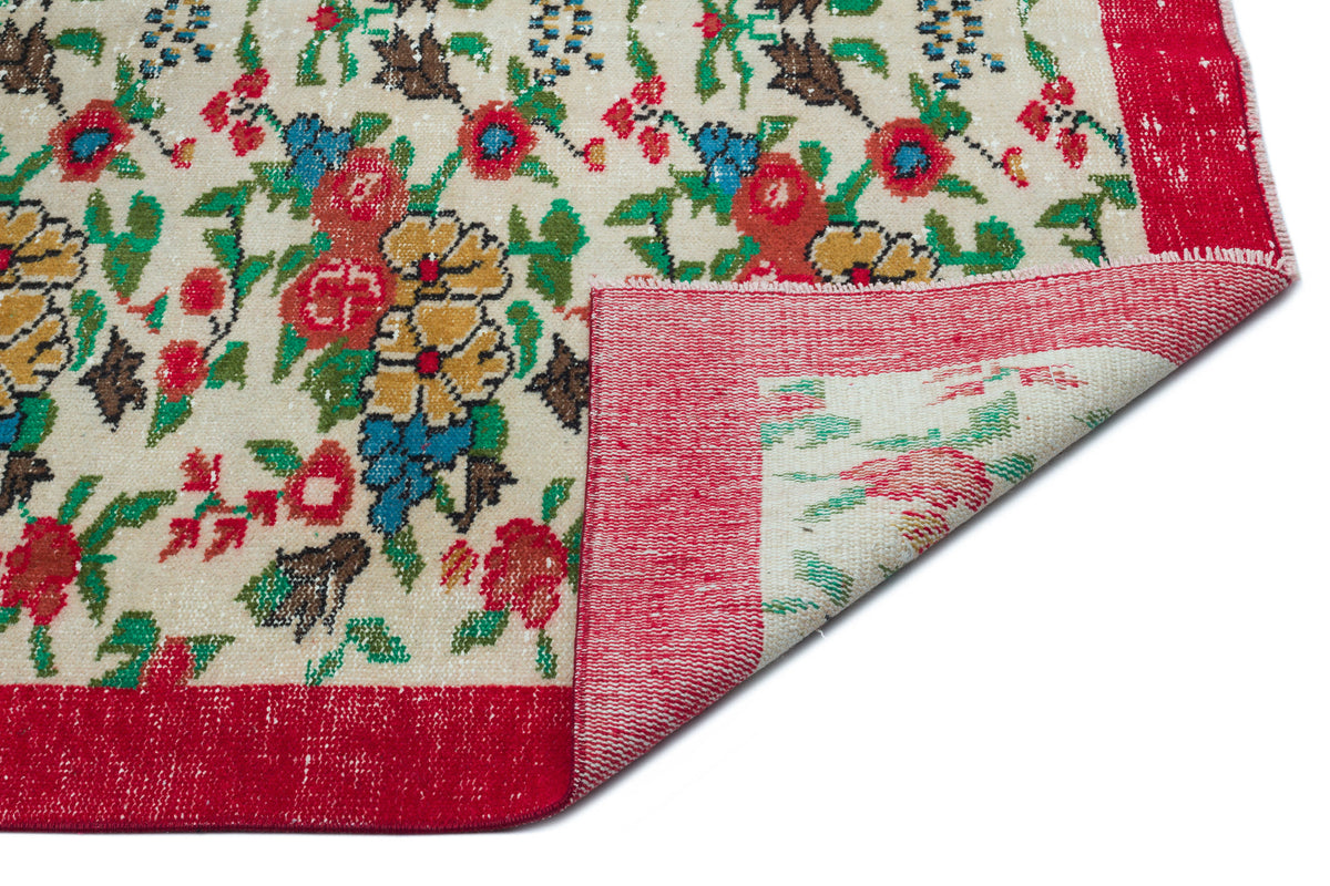 Cream rug with a multi-colored floral pattern and a wide red border, shown with a corner folded over on a white background.
