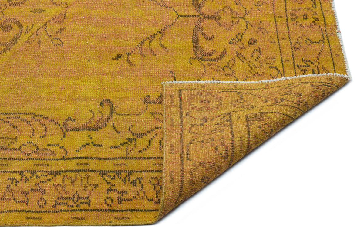 Mustard yellow vintage-style rug with a distressed brown floral pattern and a folded corner on a white background.