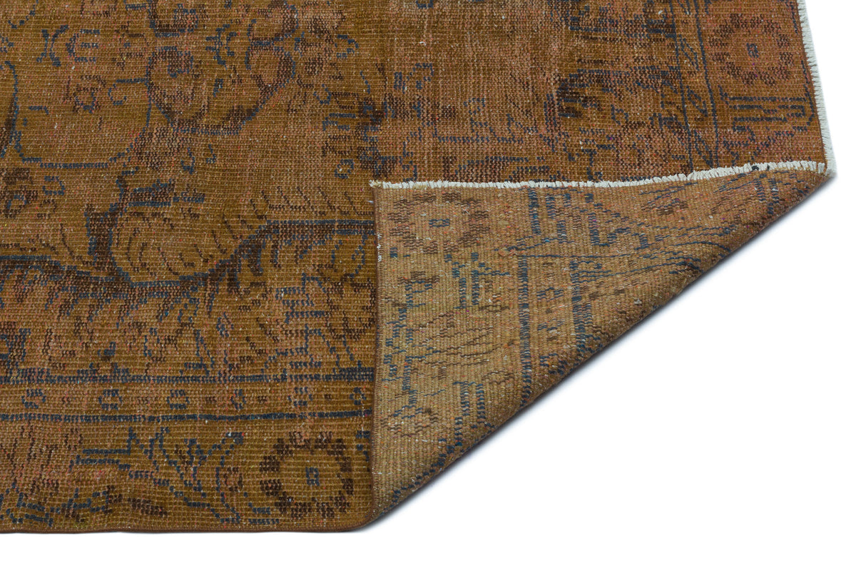 Distressed brown and blue vintage-style rug with a floral medallion pattern, shown with a corner folded over.