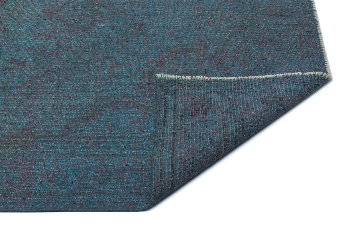 Teal textured rug with flecks of red and blue, shown with a folded corner revealing the woven backing.