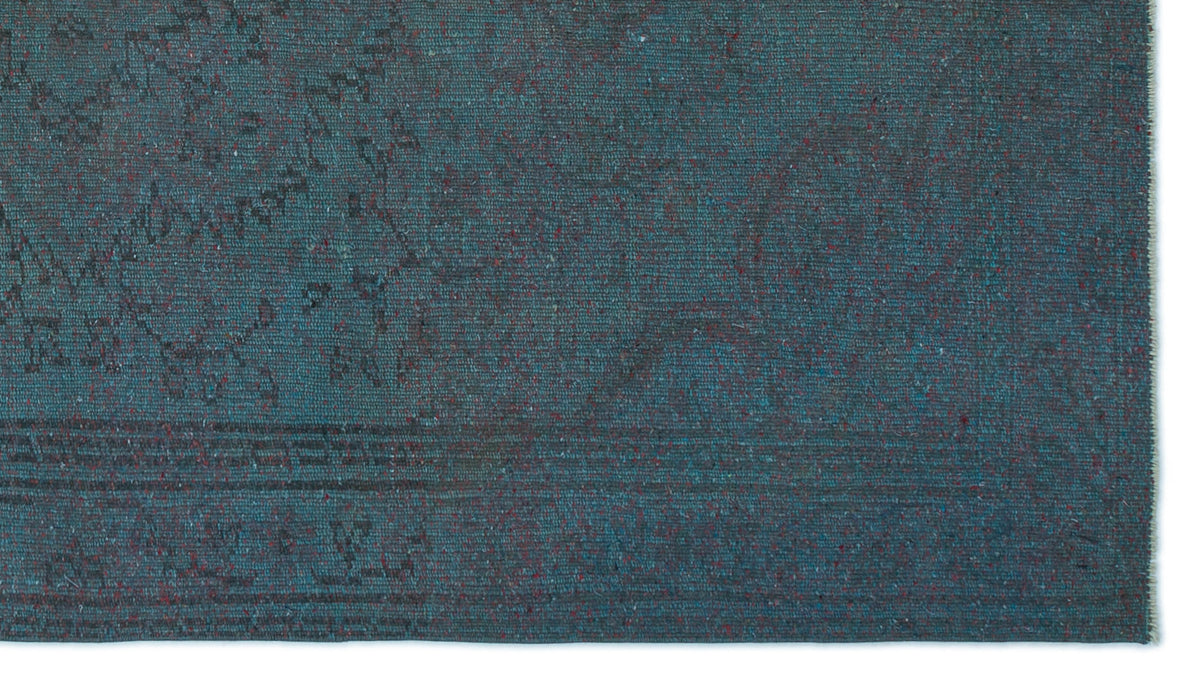 Teal and dark blue distressed rug with a faint, traditional medallion pattern and speckled red accents.