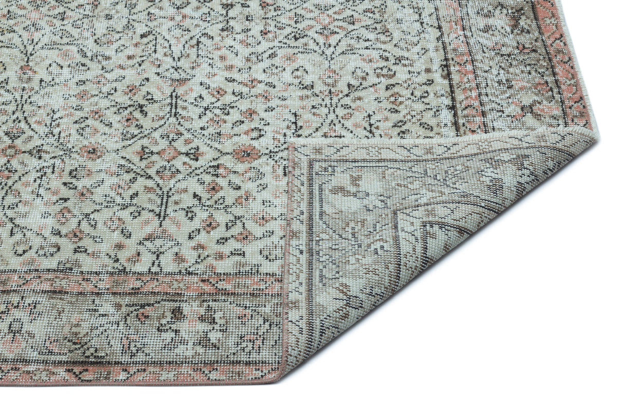 Beige and cream traditional rug with a distressed floral pattern and a folded corner, isolated on a white background.