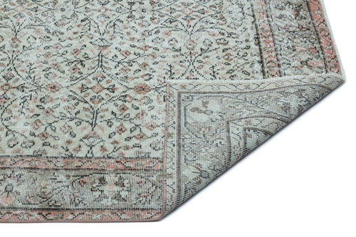 Load image 1 in gallery view. Beige and cream traditional rug with a distressed floral pattern and a folded corner, isolated on a white background.
