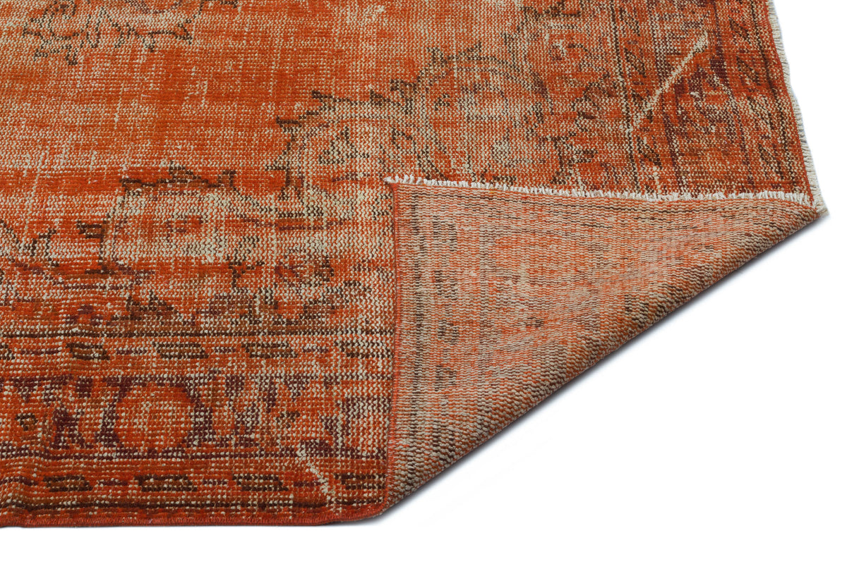 Burnt orange and cream distressed vintage-style rug with a folded corner revealing the woven backing.