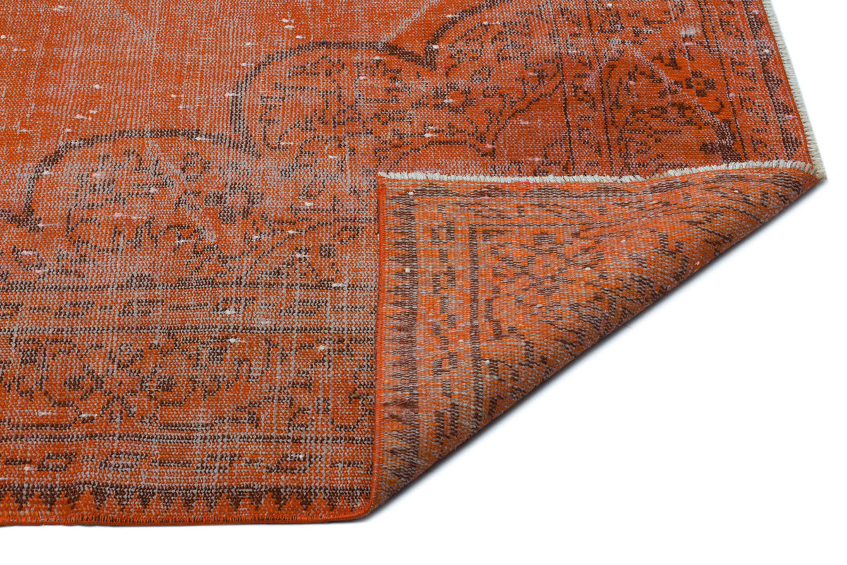 Distressed orange and brown vintage-style rug with a faded medallion pattern and a folded corner showing the underside.
