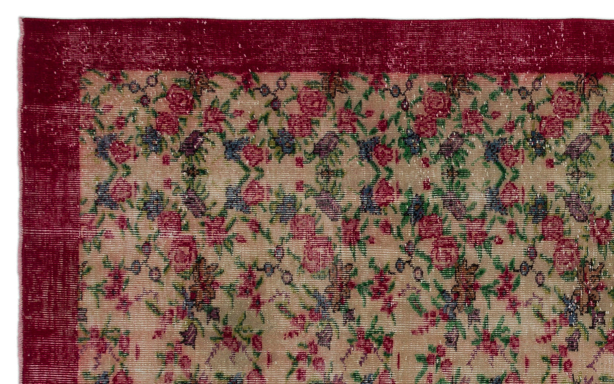 Beige rug with a distressed floral pattern in red, green, and blue, featuring a solid deep red border.