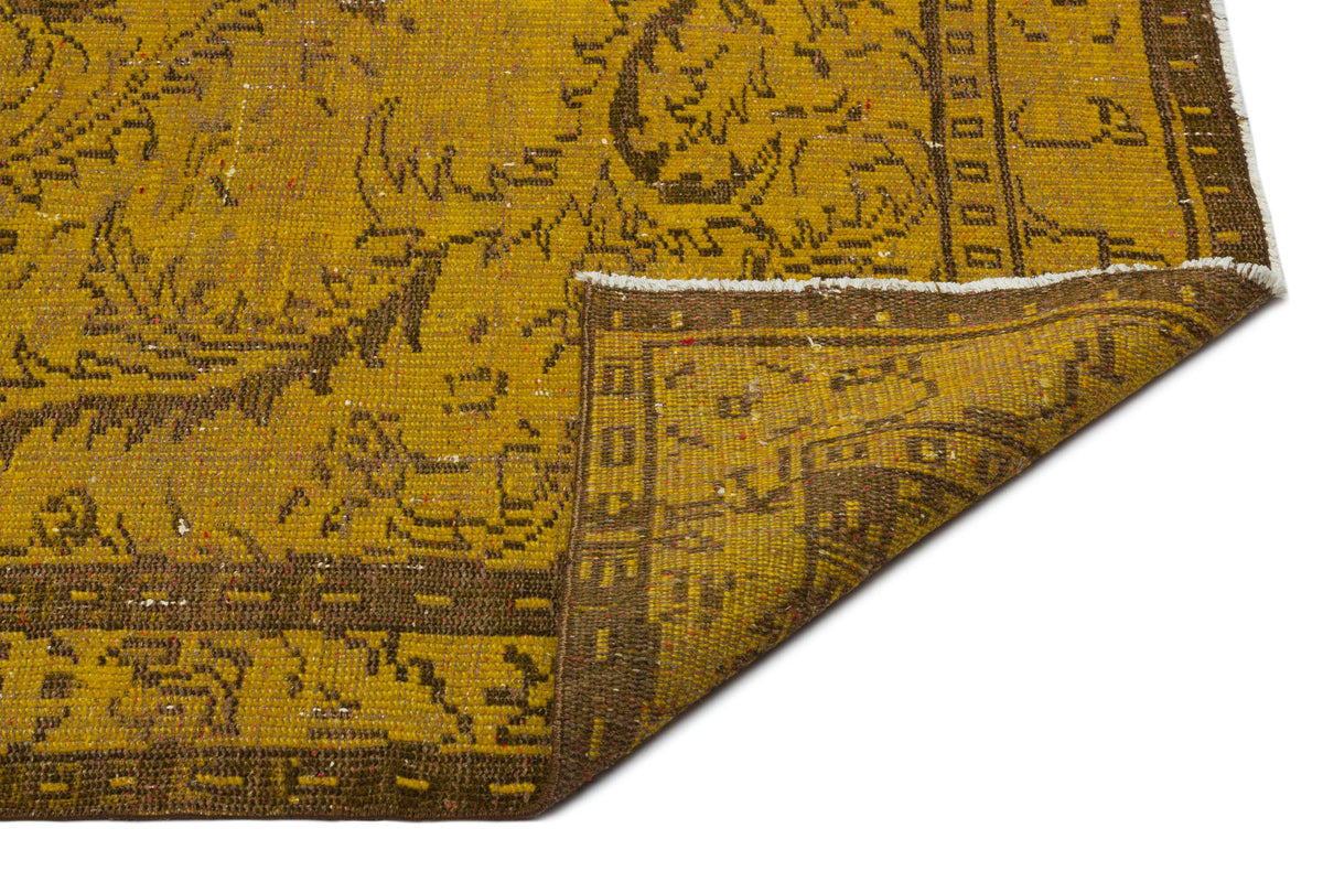 Mustard yellow and brown vintage-style rug with a distressed floral pattern and a folded corner on a white background.