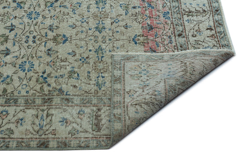 Load image 1 in gallery view. Beige vintage-style rug with a floral pattern in blue and pink, featuring a folded corner showing the woven backing.