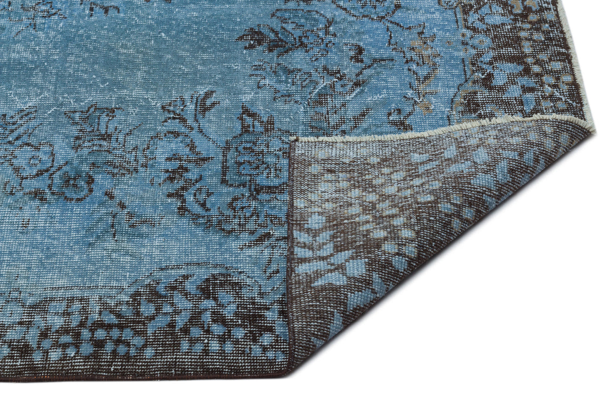 Distressed blue and brown rug with a floral pattern, shown with a corner folded to reveal the dark brown backing.